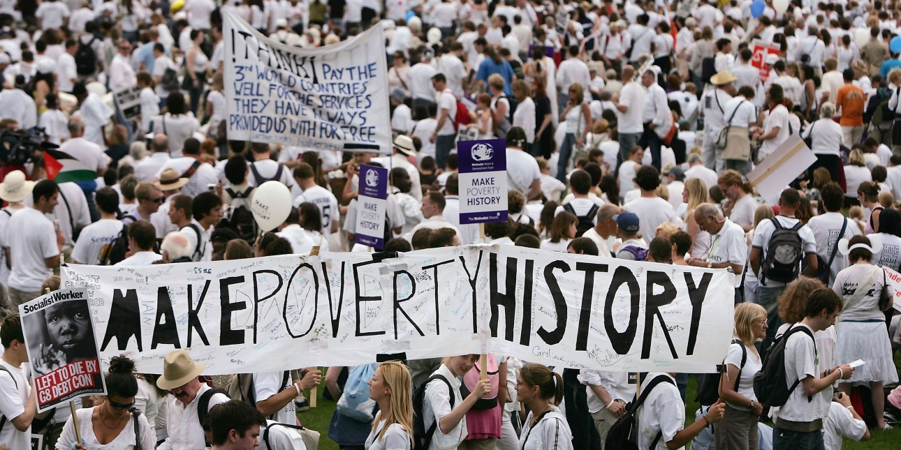 A group of people wearing white t-shirts attending a march and holding up several signs that say Make Poverty History
